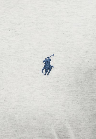 Μπλε κεντημένος παίκτης πόλο που καβαλάει άλογο κρατώντας ρόπαλο σε ανοιχτό γκρι ύφασμα φόντο.