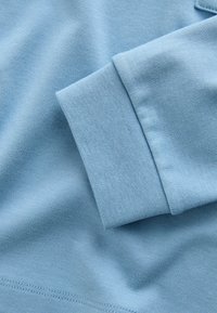 Svetlomodrá dlhá rukávová tkanina s detailom rebrového manžetu a viditeľným šitím na hladkom bavlnenom materiáli.