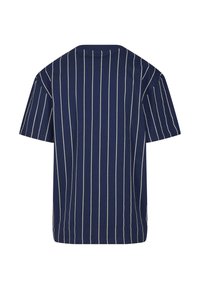 Tumši zila T-kreklā ar baltām vertikālām svītrām, īsām piedurknēm, apaļu kaklu un brīvu piegriezumu. Mīksts kokvilnas audums ar gludu tekstūru.