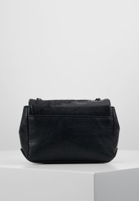 Černá kožená taška s texturou, se zipovým uzávěrem, kulatým tvarem a jemnými dekorativními detaily na vrchu. Rukojeti nejsou vidět.