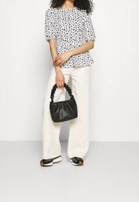Blomstret hvid bluse, brede kremfarvede bukser, sort rynket håndtaske og sorte og hvide sneakers. Glat tekstur og afslappet pasform.