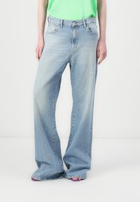 Jeans large bleus clairs en denim, avec une taille mi-haute, cinq poches et une finition délavée. Assortis avec un haut vert.