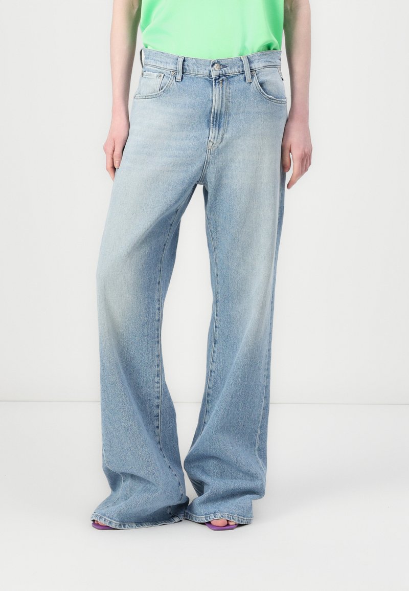 Jeans large bleus clairs en denim, avec une taille mi-haute, cinq poches et une finition délavée. Assortis avec un haut vert.