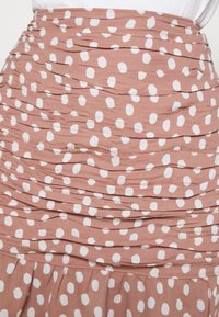 Brun kjol med vita prickar, med ett rynkat design och en flödande nedre del. Mjukt tyg med en texturerad utseende.