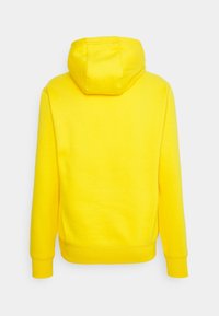 Sweat à capuche jaune vif à manches longues, vu de dos sur un fond gris clair uni.