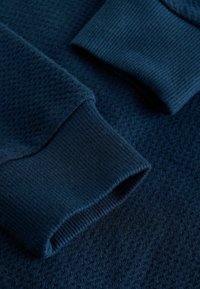 Navy blue textile featuring a honeycomb pattern with ribbed cuffs. The texture appears soft and comfortable with a smooth finish.