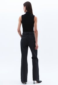 Musta ilmanhiha toppi yhdistettynä korkeavyötäröisiin tummiin farkkuihin. Farkuissa on suora lahje ja hienovaraiset tekstuuriyksityiskohdat.