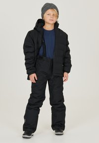 Svart pufferjacka med huva, tillsammans med svarta snöbyxor. Modellen har på sig en marinblå skjorta under och en grå stickad beanie. Hållbart tyg och design.