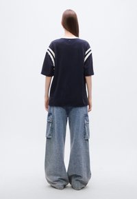 Μπλε σκούρο oversized t-shirt με λευκές ρίγες στα μανίκια, συνδυασμένο με φαρδιά, ανοιχτό μπλε τζιν παντελόνια cargo με πλαϊνές τσέπες.