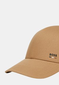 Cappellino da baseball color sabbia realizzato in tessuto testurizzato, con visiera curva e logo "BOSS" nero con accenti bianchi e arancioni.