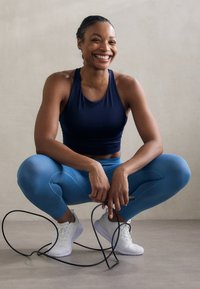 Leggings sportivi blu e una canotta navy con finitura testurizzata, abbinate a scarpe da ginnastica bianche, accanto a una corda per saltare nera su un pavimento liscio.