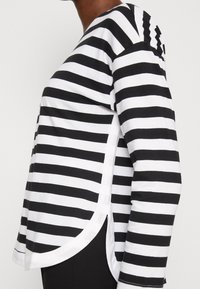 Schwarz-weißer gestreifter Langarmshirt mit abgerundetem Saum, seitlichen Schlitzen und weichem Baumwollstoff, an den Schultern eng anliegend und locker am Körper.