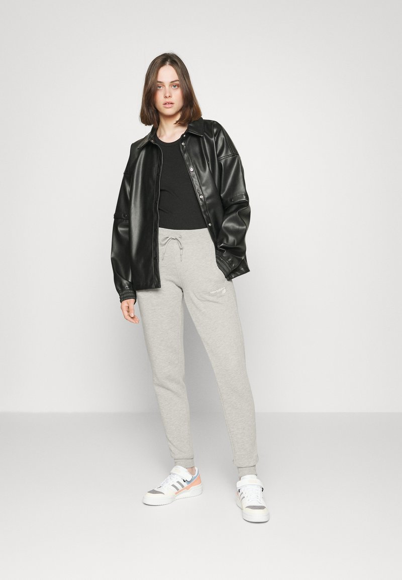 Chaqueta de cuero sintético negra, camiseta negra, pantalones de chándal grises y zapatillas multicolor. Atuendo sencillo y casual con un ajuste holgado.