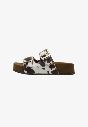 Brown and white cow-print slide sandal with two adjustable straps, gold metal buckles, and a textured brown footbed. Flat, rubber sole.