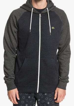 Reißverschluss-Hoodie mit marineblauem Körper und dunkelgrauen Raglanärmeln, weißen Kordeln, Fronttaschen und einem kleinen Logo auf der Brust.