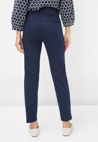Marineblaue Slim-Fit-Hosen mit mittlerer Leibhöhe, Gesäßtaschen und glatter Textur. Getragen mit hellen Schuhen und einem gemusterten Oberteil.