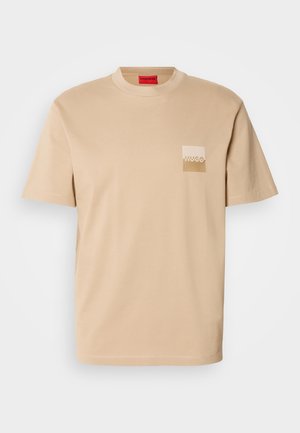 Beige cotton t-shirt with a crew neck. Features a small square logo pocket in a lighter shade, with embossed text. Short sleeves.