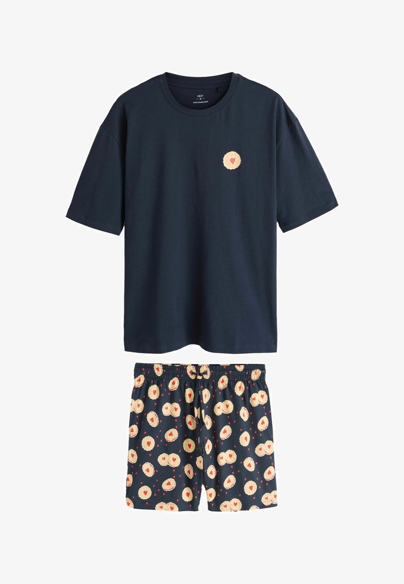 Marineblå kortærmet t-shirt i bomuld med et hjerte-mønsteret patch, kombineret med mønstrede pyjamas-shorts med creme- og røde hjertedesign.