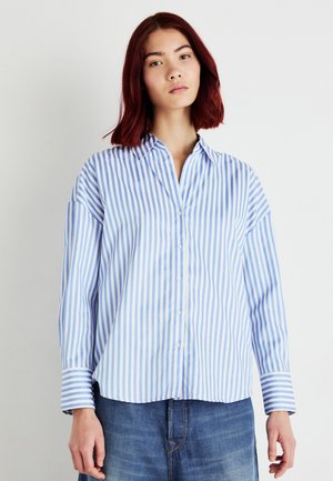 Chemise à rayures verticales bleu et blanc à manches longues avec col, fermeture à boutons sur le devant et larges poignets. Tissu en coton doux.
