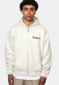 Sweat à capuche zippé blanc en matière douce avec une poche avant, des poignets côtelés et le texte "Dropsize" brodé en noir sur la poitrine.