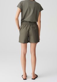 Olivově zelený top s krátkým rukávem spárovaný s odpovídajícími šortkami; elastický pas a uvolněný střih; hladká textura; jednoduchý design; ploché černé sandály.