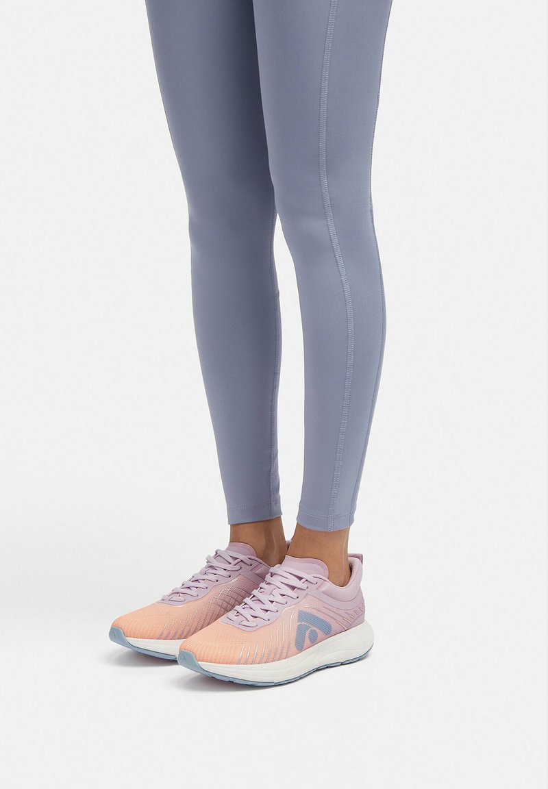 Lichte hardloopschoenen in een vervagend roze en lila met een gestructureerde mesh bovenkant, paarse veters en een flexibele witte zool, gecombineerd met grijze leggings.