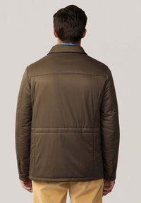 Chaqueta acolchada marrón con un cuello estructurado, costuras horizontales y puños con botones, vista desde la parte de atrás. Tejido texturizado.