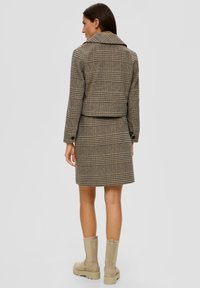 Brązowa kurtka w kratkę z kołnierzykiem, w zestawie ze spódnicą w tym samym stylu. Całość wykonana z teksturowanej tkaniny, z beżowymi botkami do kolan.