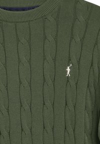 Grön kabelstickad tröja med ribbad halsringning och en liten broderad logga i vitt på vänster bröst.