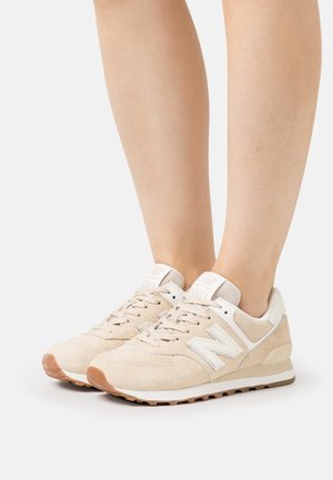 Zapatillas de ante beige con un logotipo blanco de "N", diseño con cordones, suela de goma y cuello acolchado, con acentos texturizados.