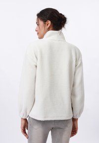 White fleece pullover with a high collar, balloon sleeves, and textured fabric. Smooth finish with no visible patterns or hardware accents.