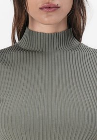 Olivgrüner gerippter Rollkragenpullover aus weichem, elastischem Stoff. Verfügt über einen hohen Kragen und eine figurbetonte Passform mit horizontaler Rippstruktur.