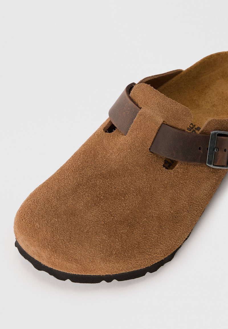 Sabots en daim marron avec une bride en cuir marron foncé et une boucle, bout rond et surface texturée pour une meilleure adhérence.