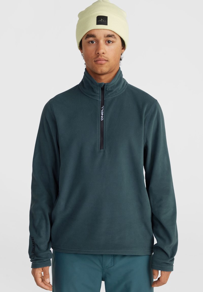 Tume teal fliisist kootud pullover kõrge krae, pooltõmmete ja musta tõmblukuga. Rinnas on logo ja varrukatel on sõrmeauk.