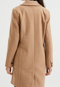 Brown wool-blend coat featuring a tailored design, double-breasted buttons, and a notched collar. Equipped with side pockets and a smooth texture.