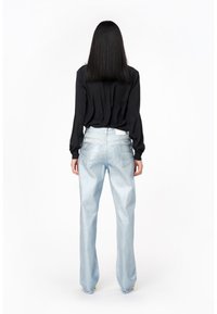 Blusa nera a maniche lunghe abbinata a jeans a gamba larga di un delicato blu chiaro. I jeans presentano tasche posteriori e una leggera lucentezza. Dettaglio della vita bianca visibile.