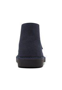 Botas de tobillo de ante azul marino con un acabado suave, punta redondeada y suela de goma negra; presentan un diseño minimalista sin herrajes visibles.