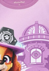 Lila Kinder-T-Shirt mit einer Figur, die einen rosa Hut und ein Abzeichen-Emblem trägt. Der Hintergrund zeigt ein stilisiertes Gebäude in ähnlichen Farben.