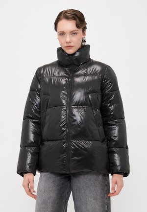 Doudoune noire et brillante avec un col haut, zip et design matelassé. Elle possède de grandes poches et des poignets élastiques.