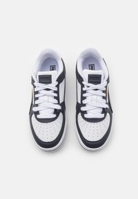 Baskets blanches et bleu marine avec une tige en cuir texturé et mesh, bout perforé, lacets plats blancs et une étiquette logo sur la languette.