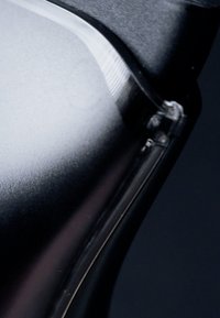 Gros plan sur un objet en plastique noir translucide aux bords incurvés et à la surface lisse et réfléchissante sur un fond sombre.