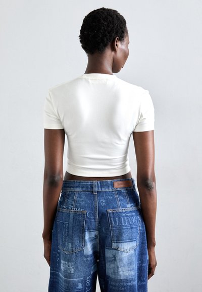 Biely krátky rukáv crop top v kombinácii s modrými džínsami s potlačou a dvoma zadnými vreckami. Hladký bavlnený materiál.