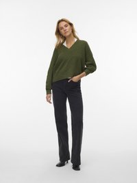 Green v-neck sweater with a loose fit, worn over a white top, paired with black straight-leg jeans and black ankle boots.