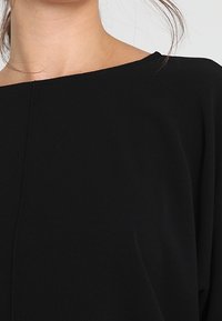 Svart topp med vid halsringning, mjukt material och löst/snabbt passar. Har en ren, enkel design utan synliga knäppningar eller dekorationer.