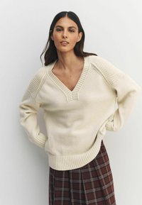 Kreemja värvi kudumitega särk V-kaelusega, soonikute äärtega ja lõdva stiiliga, koos pruunist ruudulise seelikuga.