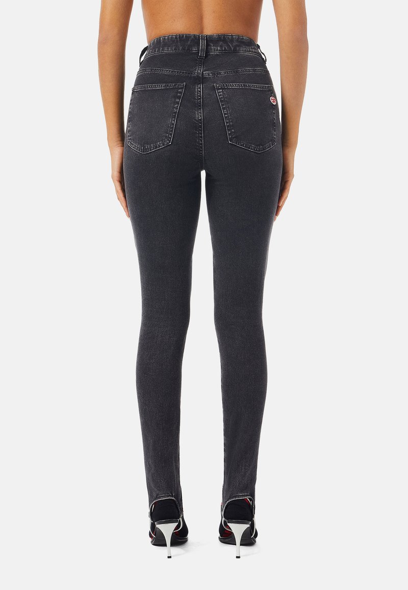 Donna che indossa jeans skinny grigi scuri a vita alta e scarpe con tacco nere, vista di spalle su uno sfondo semplice.