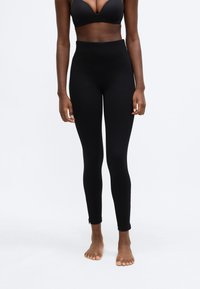 Højtaljede sorte leggins lavet af strækbart materiale, med et tætsiddende design og lynlåse ved anklerne for nem påklædning.