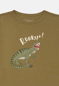 Olivegrünes Baumwoll-T-Shirt mit einer Grafik eines brüllenden Dinosauriers mit Zähnen, zusammen mit dem Text "ROARR!!" in Weiß. Kurzärmliges Design.