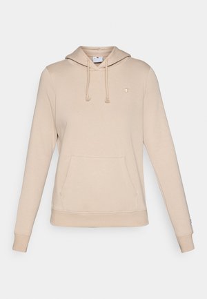 Beige krēslā aizdares kapučšvītra, kas izgatavota no mīksta auduma, ar priekšējo kabatu, ribinātiem aprocēm un mazu logotipu uz krūtīm.