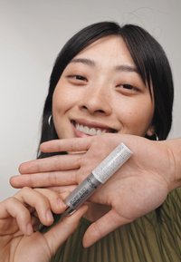 L'Oréal Plump & Set Brow Artist dans un tube argenté élégant avec un capuchon blanc affichant un texte en relief ; finition brillante ; tenu dans une main contre un fond clair.